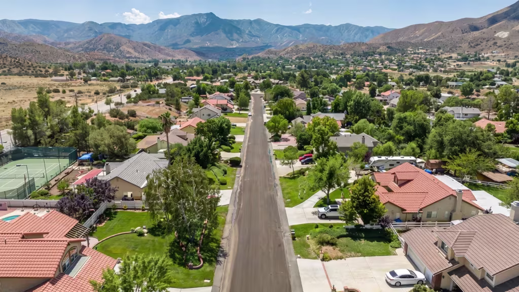 Acton spreads across a residential valley set beneath a rugged mountain backdrop, seen from high aerial oblique