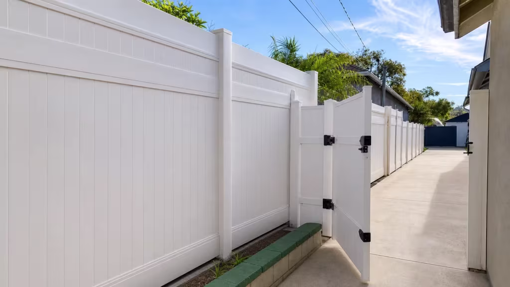 Visible drainage channels mark the concrete driveway crossed by this Tan vinyl privacy fence and gate in Glendale