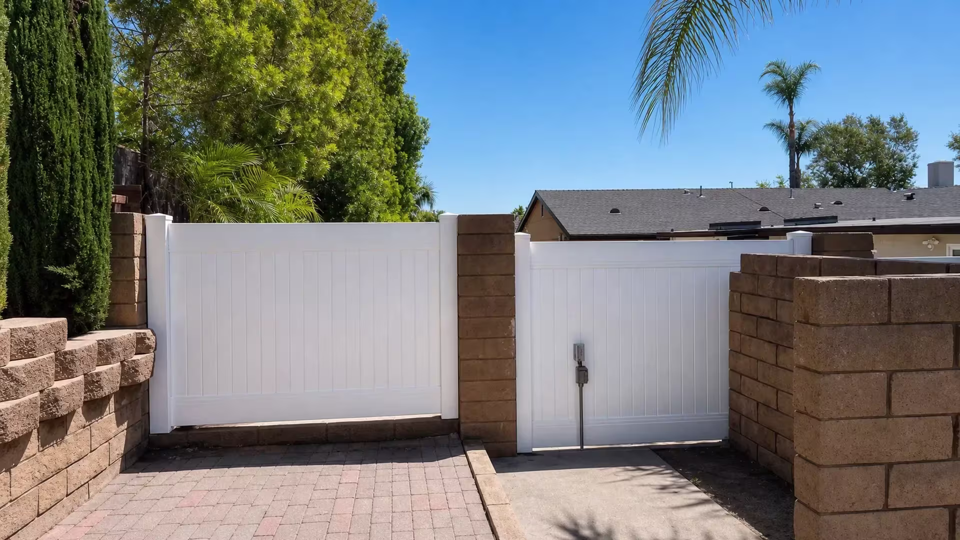 A palm-lined path runs beside this White vinyl privacy fence, its gate set between masonry columns in Yorba Linda