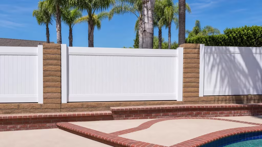 White vinyl privacy fence infill set between tan split-face masonry columns near a pool in Yorba Linda