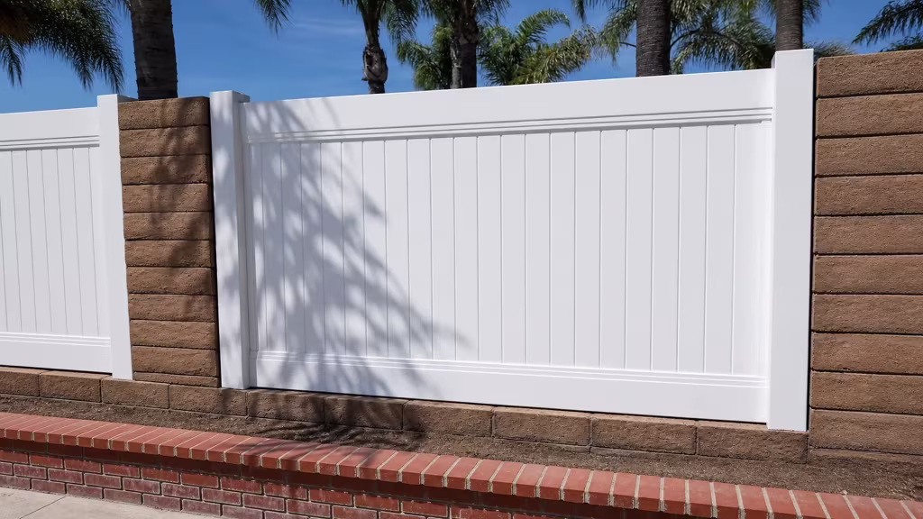 Mature palm trunks rise behind this White vinyl privacy fence set on a brick-edged retaining wall in Yorba Linda