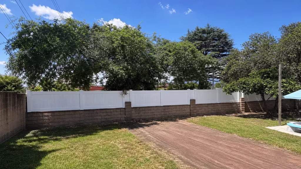 White vinyl privacy wall topper edging a pool corner beneath a turquoise umbrella and mature trees