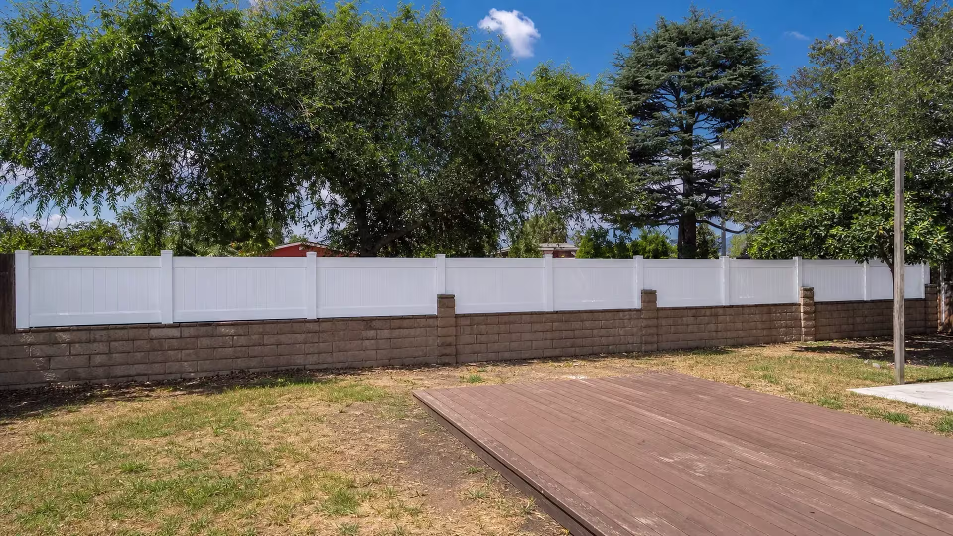 Masonry pilasters and broadleaf trees frame this Azusa yard's continuous White vinyl wall topper, built for privacy