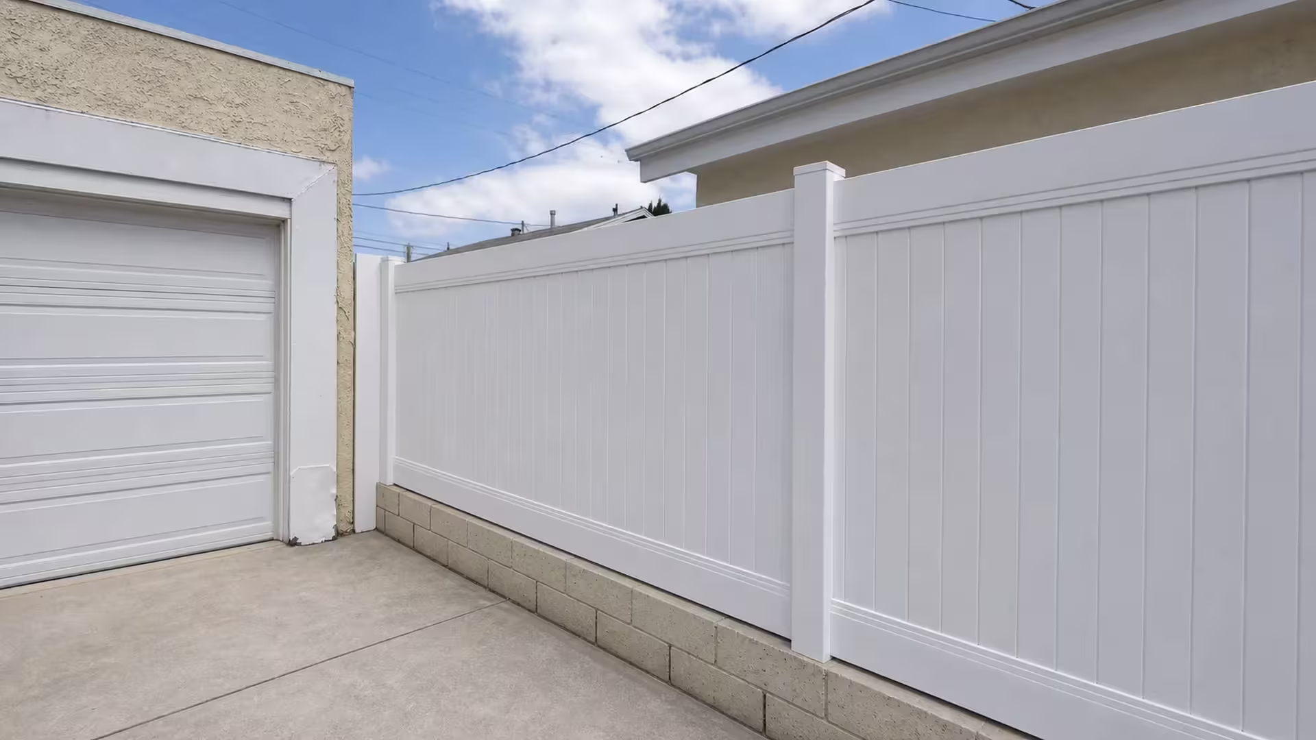 A beige block wall carries this White vinyl privacy fence past a stucco garage in Culver City