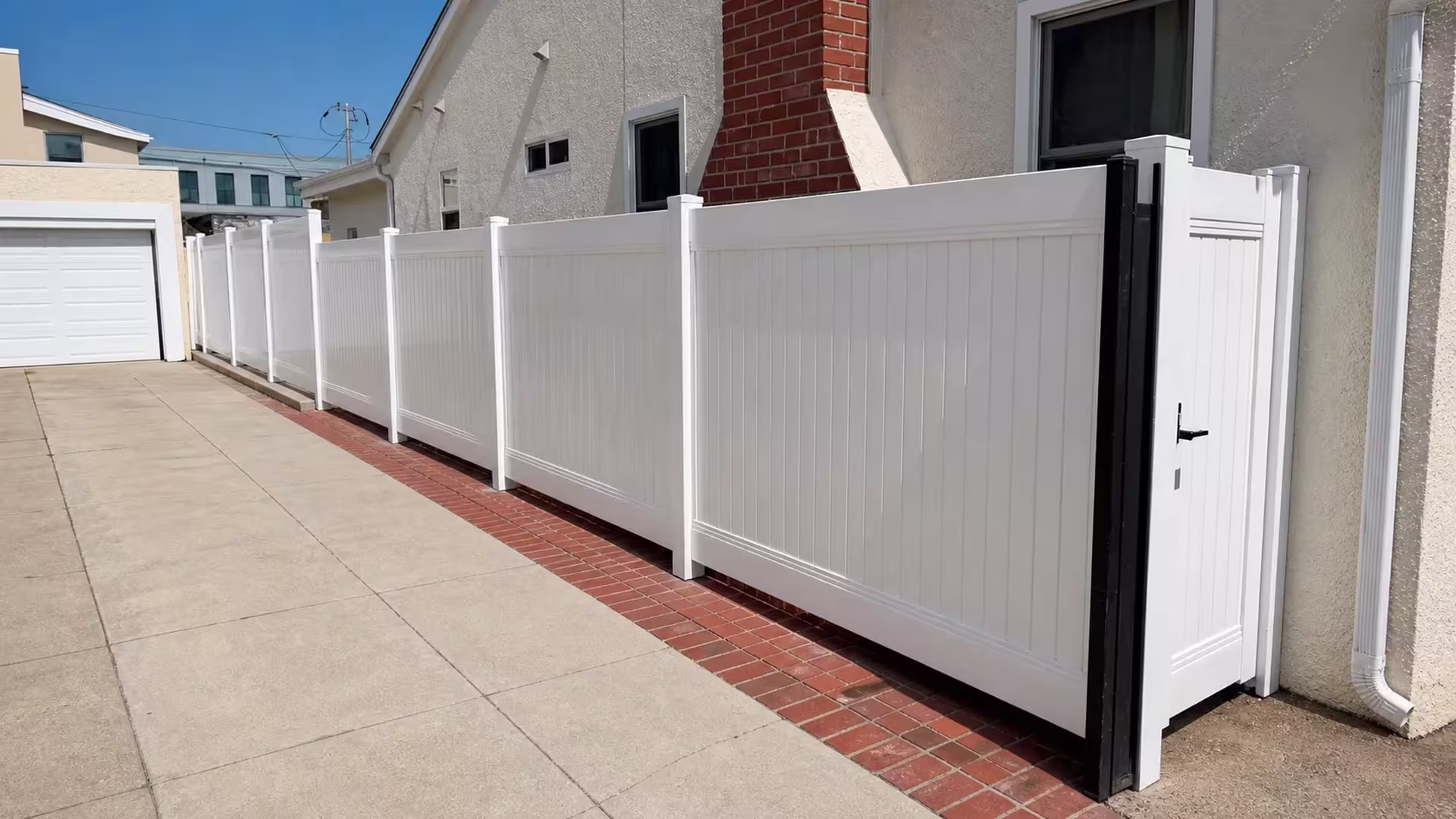 A cream stucco wall and red brick chimney frame this White vinyl privacy fence in Culver City