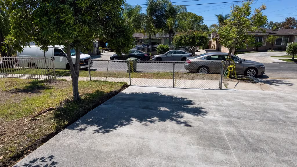 Before installation, a chain-link gate crosses the front driveway beside a tree-shaded yard.