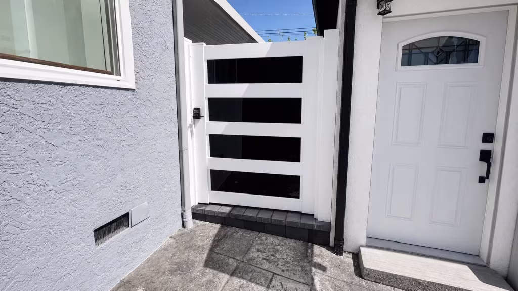 White vinyl privacy gate with dark acrylic accents fitted between a stucco house wall and a masonry wall