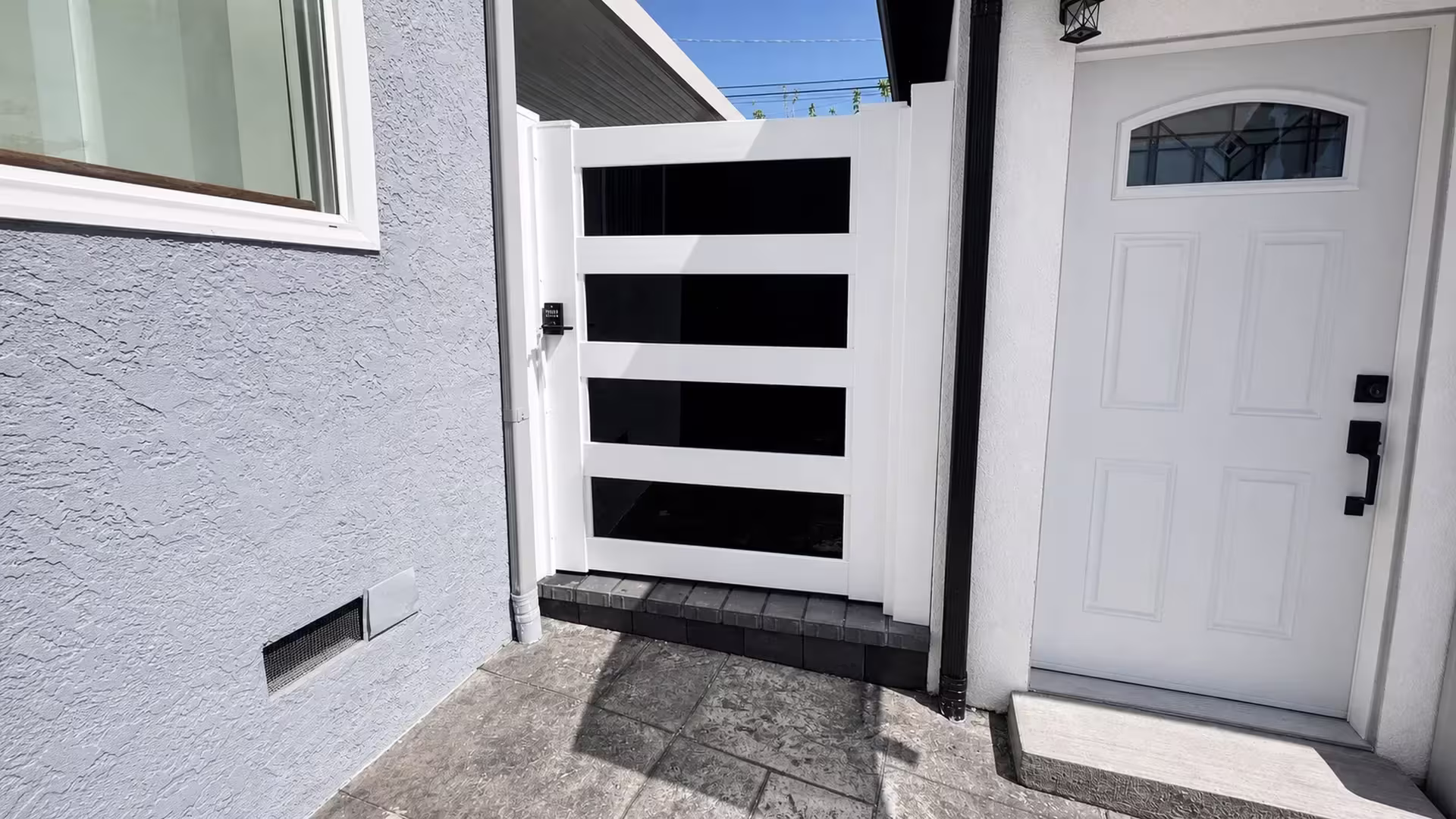 White vinyl privacy gate with dark acrylic accents fitted between a stucco house wall and a masonry wall