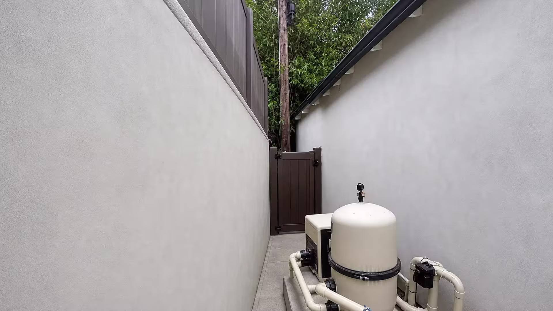 Dark Walnut vinyl wall topper adds privacy above a pool filtration pad beside dense bamboo and a utility pole