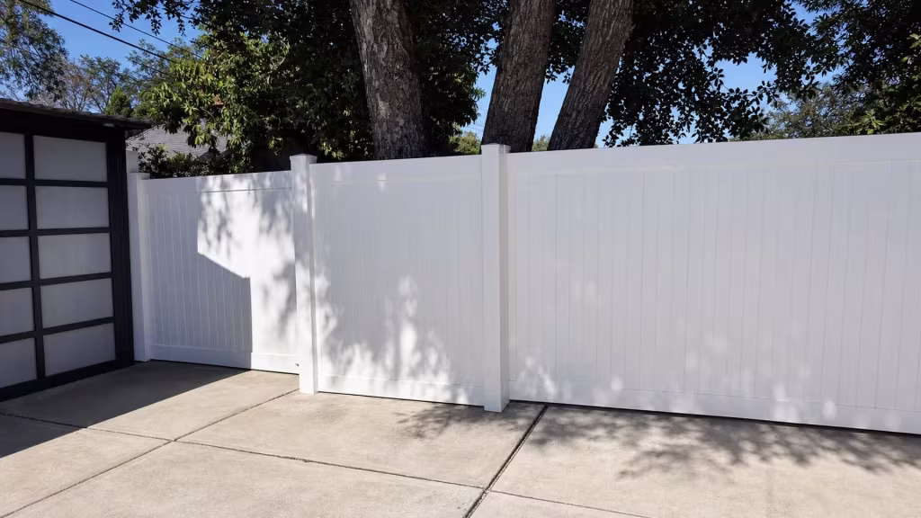 White vinyl privacy fence tracing a concrete side passage beneath a mature multi-trunk tree in Pasadena