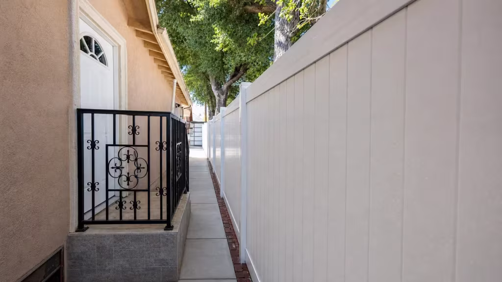 A scrolled black iron rail marks the masonry landing beside this White vinyl privacy fence in Pasadena