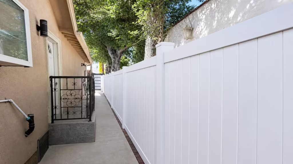 Brick edging borders the narrow concrete walkway lined by this White vinyl privacy fence in Pasadena