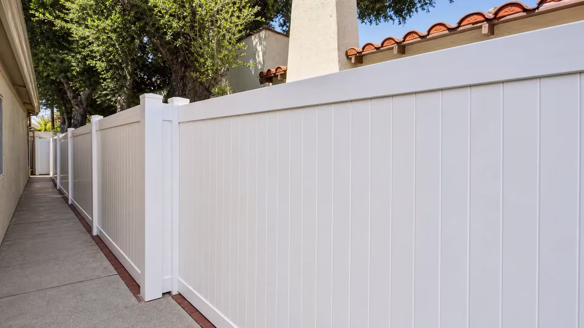 A terracotta roofline and stucco chimney rise behind this White vinyl privacy fence in Pasadena