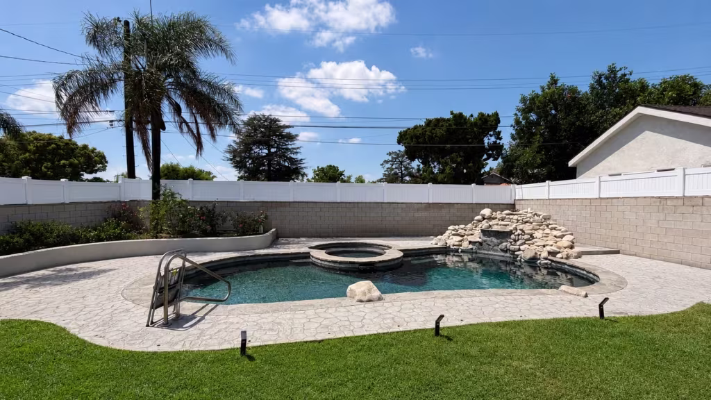 A rock waterfall and raised spa sit beside this White vinyl privacy wall topper turning toward a Burbank pool deck