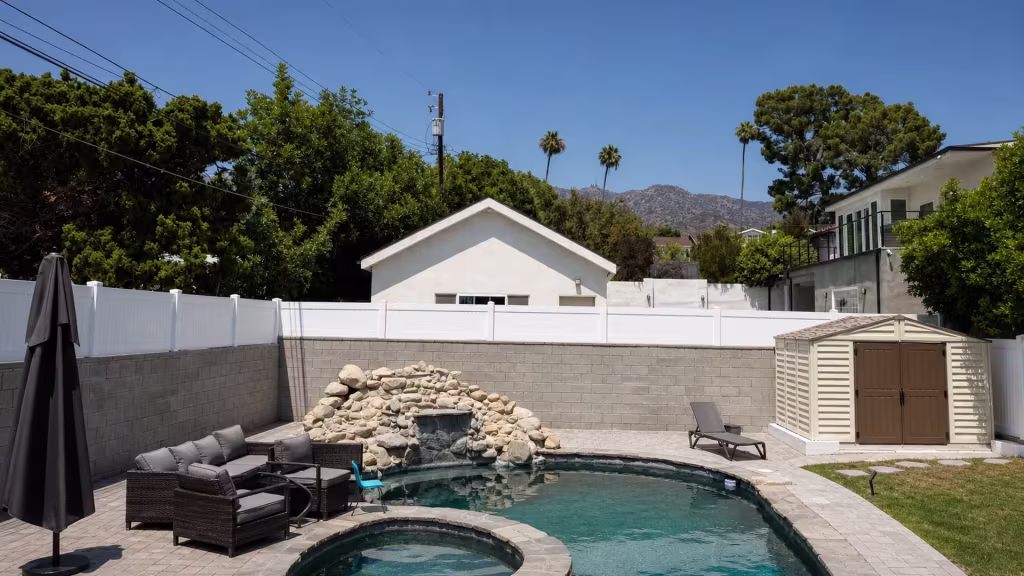 Distant mountains rise beyond a beige storage shed flanking this continuous White vinyl privacy wall topper