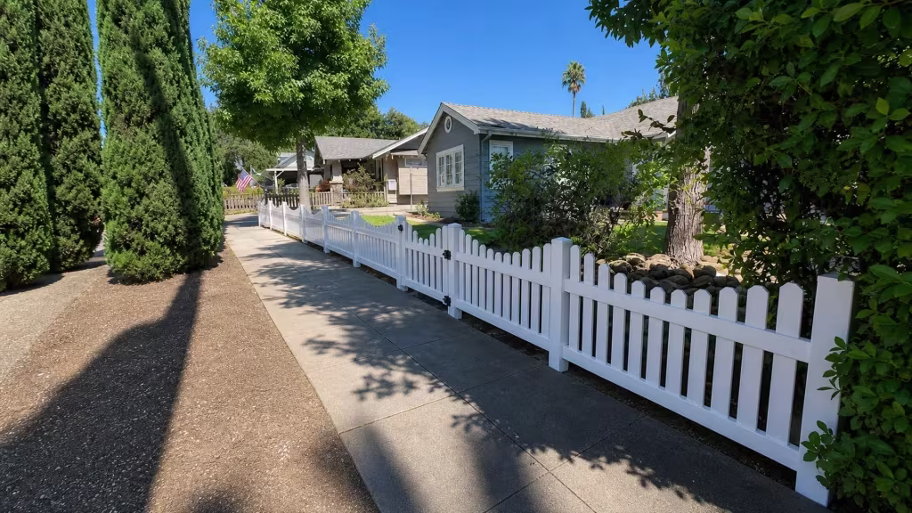 Mature columnar evergreens line a Pasadena driveway beside this scalloped White vertical vinyl picket fence