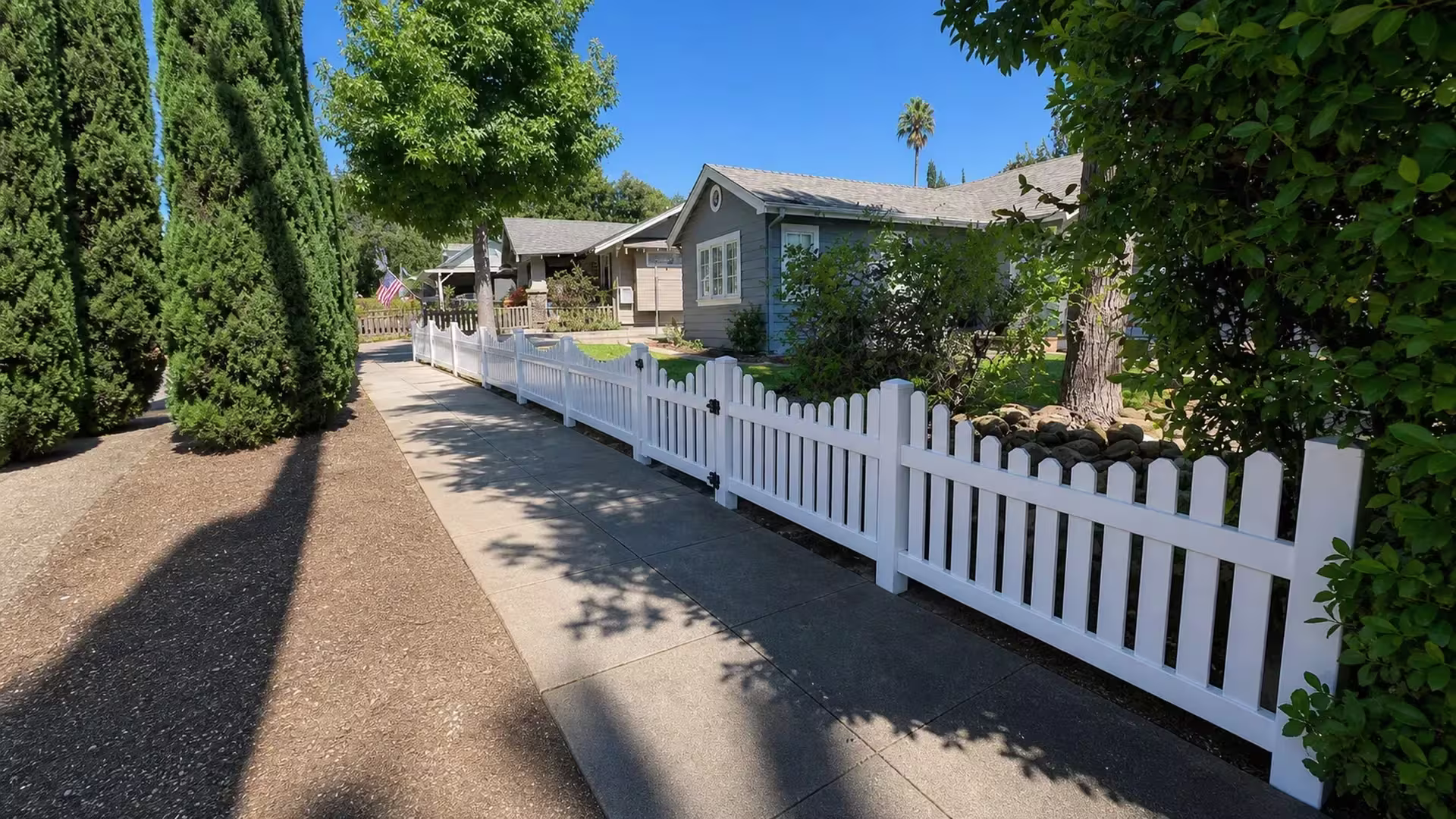 Mature columnar evergreens line a Pasadena driveway beside this scalloped White vertical vinyl picket fence