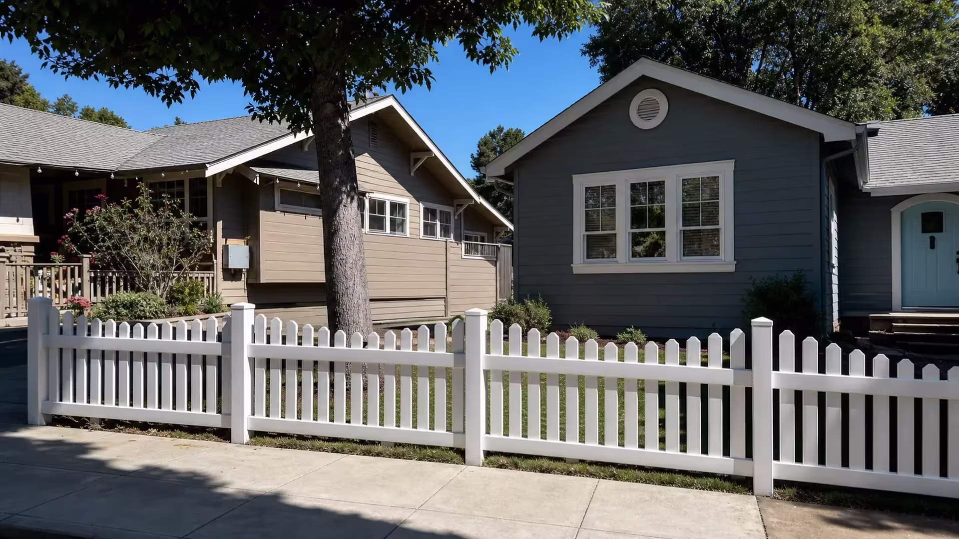 A large tree canopy shades this Pasadena front lawn behind the White vertical vinyl picket fence