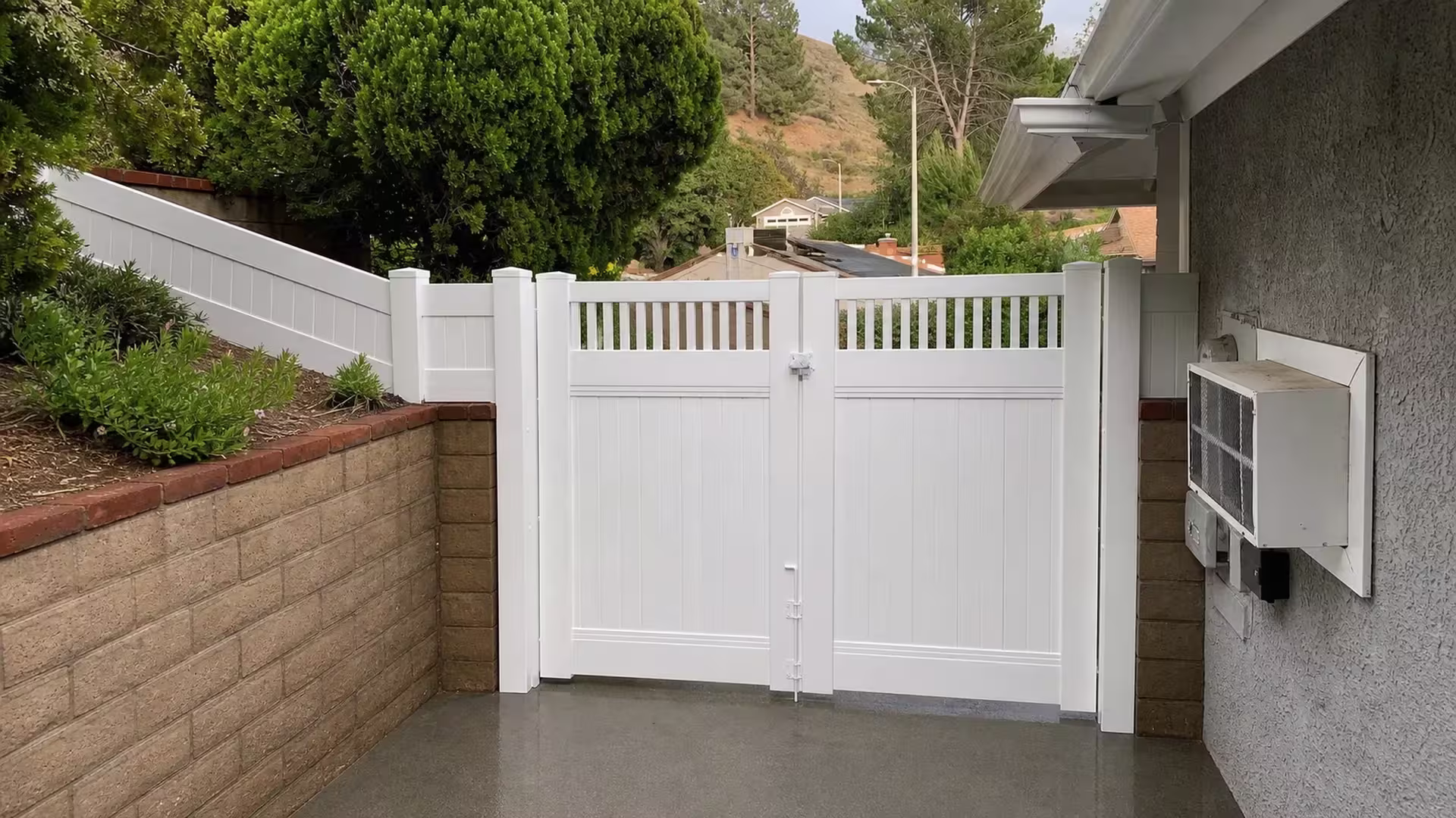 Evergreens climb the bank beside this White vinyl picket top fence gate on the Santa Clarita hillside