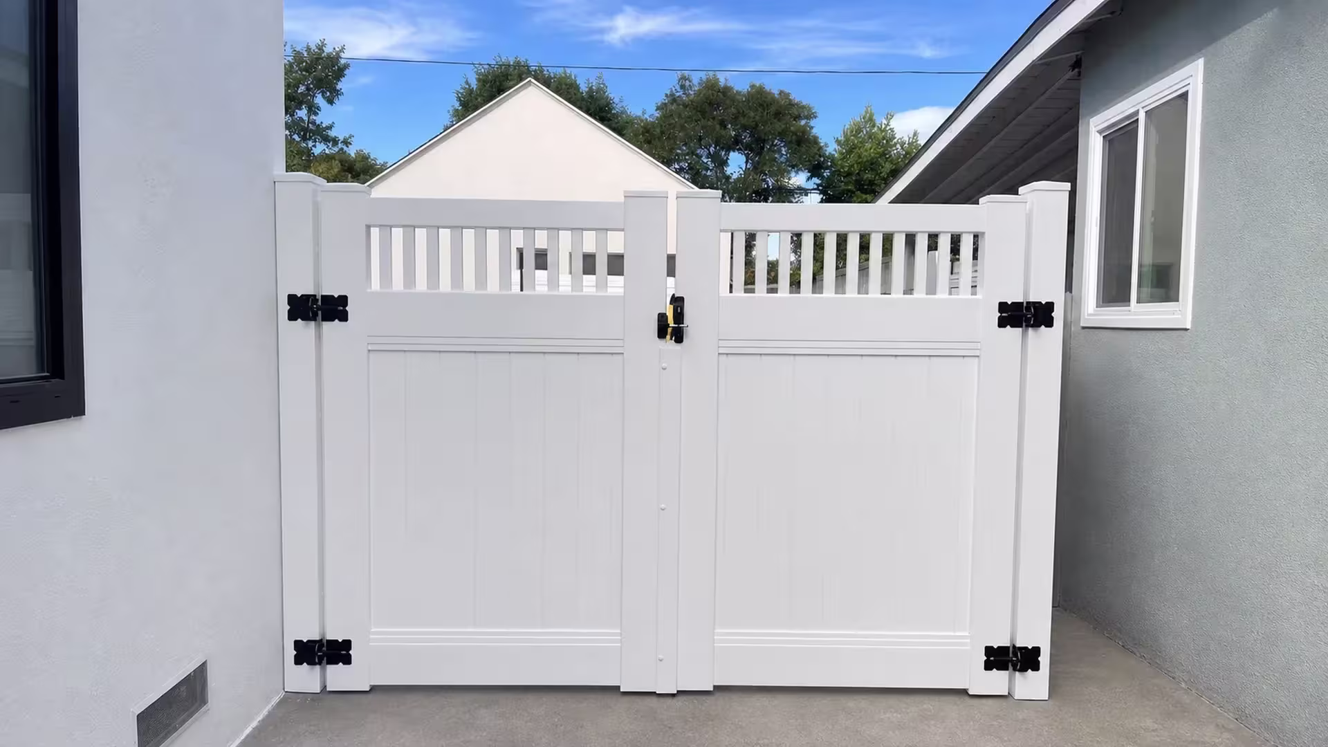 Pale blue-gray stucco on the right and White stucco on the left flank a picket-topped White vinyl privacy double gate