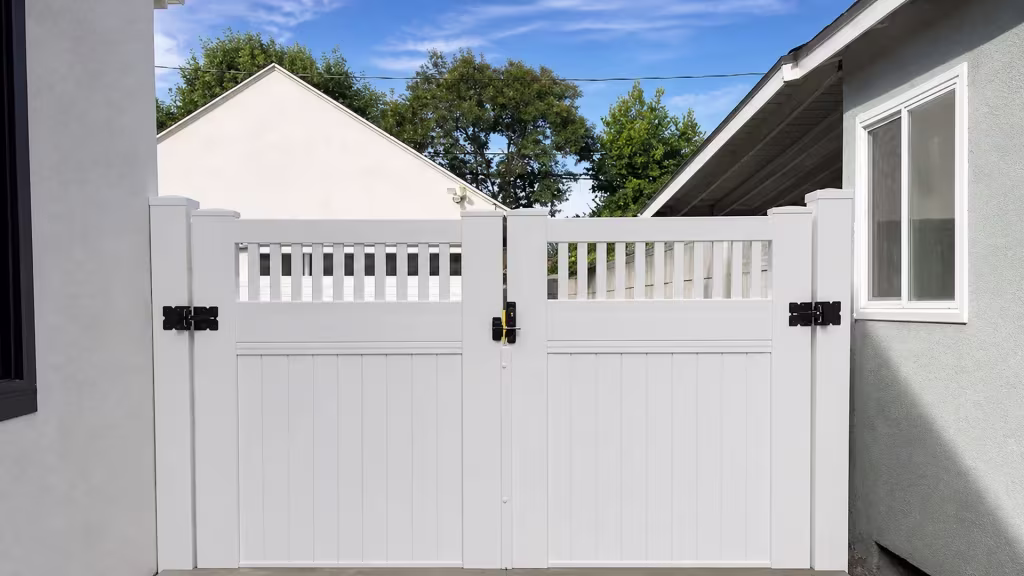 White vinyl privacy double gate with a picket top set beneath close eaves in a narrow side yard between two houses