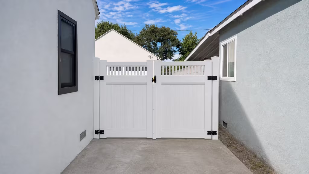 White vinyl double gate topped with pickets, spanning a narrow concrete passage toward a cream rear building