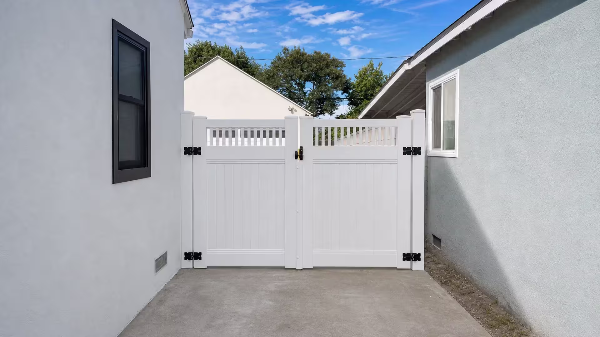 White vinyl double gate topped with pickets, spanning a narrow concrete passage toward a cream rear building