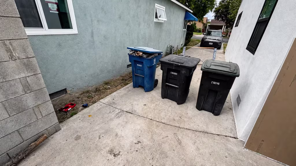 Before installation, an open side driveway between two houses contains trash bins, a dirt strip, and a parked car.