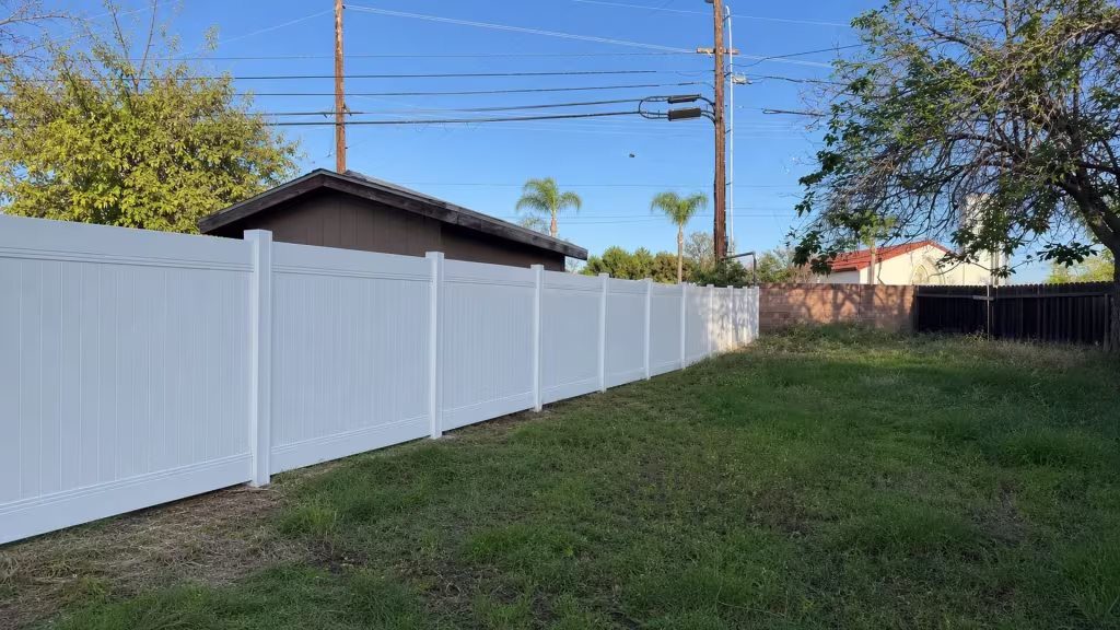 This White vinyl privacy fence follows an uneven grassy yard along the left boundary in Orange