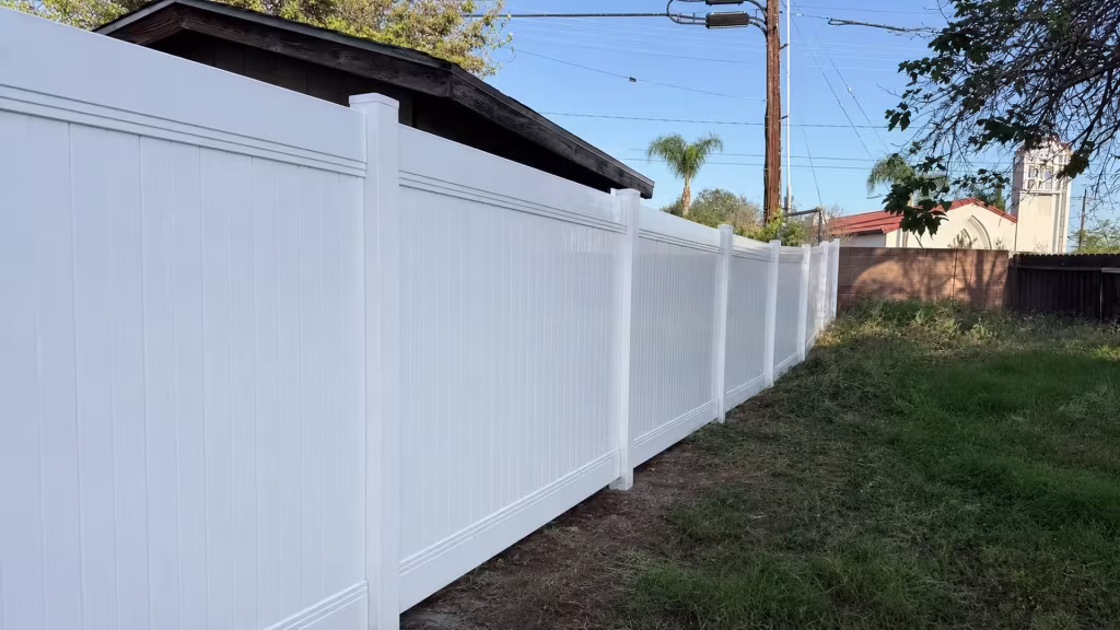 Tongue and groove boards give this White vinyl privacy fence a tall solid line past a weathered wood remnant in Orange