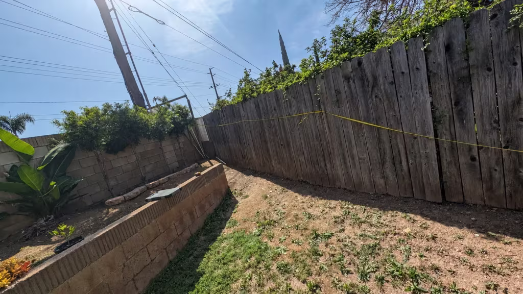 Before installation, a weathered wood fence borders a bare sloped yard and low retaining wall.