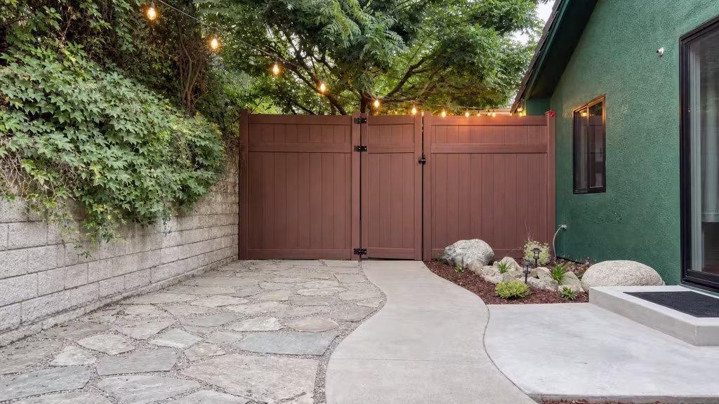 A mature tree and planting bed line the hardscape where this Dark Walnut vinyl fence gate closes a Thousand Oaks courtyard
