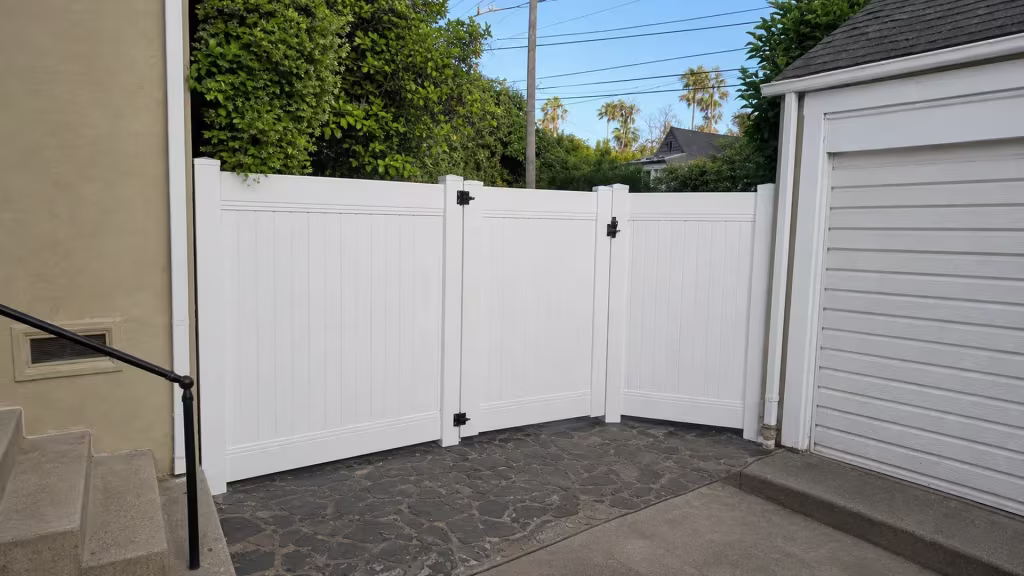 Flagstone paving meets the driveway where this White vinyl privacy fence and gate angle toward a detached garage in Pasadena