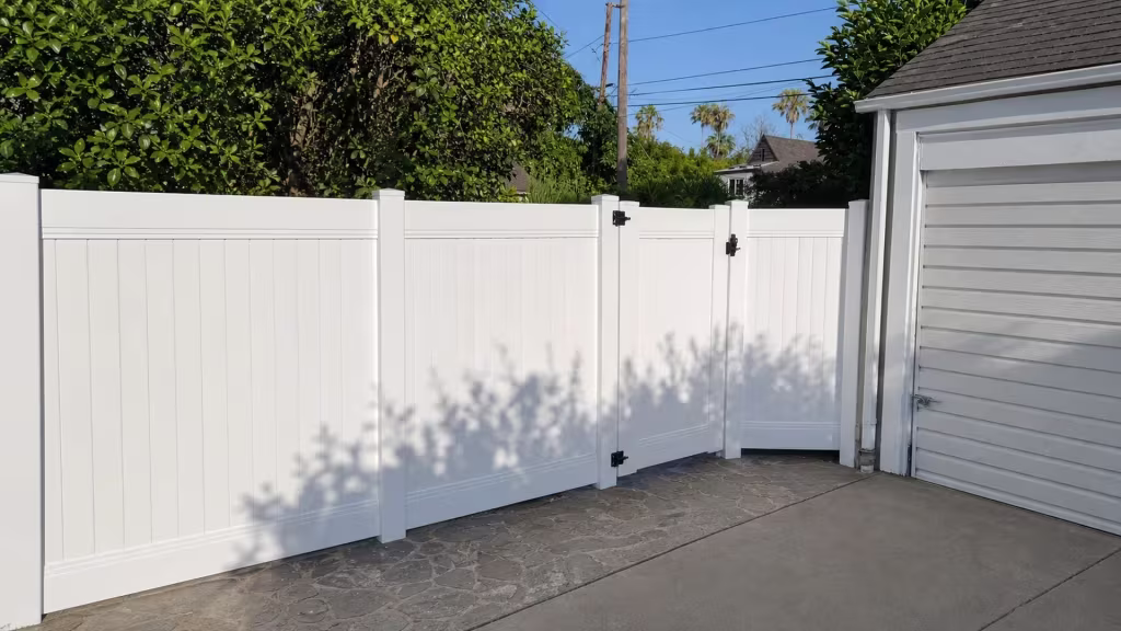 Stone and concrete paving meet at a diagonal beneath this White vinyl privacy fence in Pasadena
