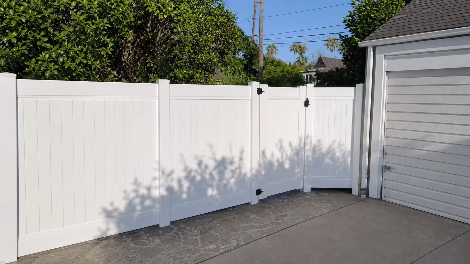 Stone and concrete paving meet at a diagonal beneath this White vinyl privacy fence in Pasadena