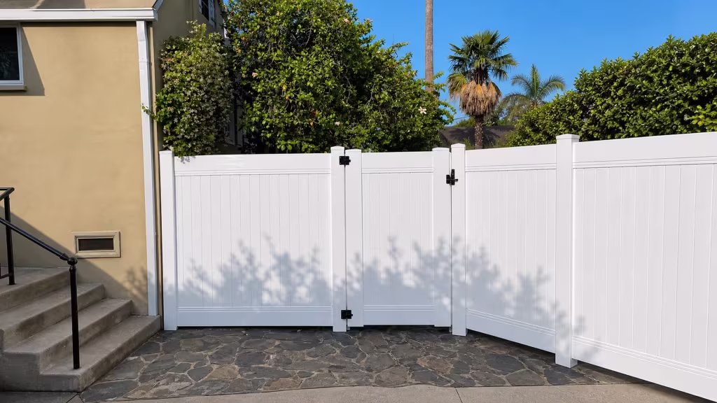 A stone side patio meets this White vinyl privacy fence and gate beside a tan stucco house in Pasadena