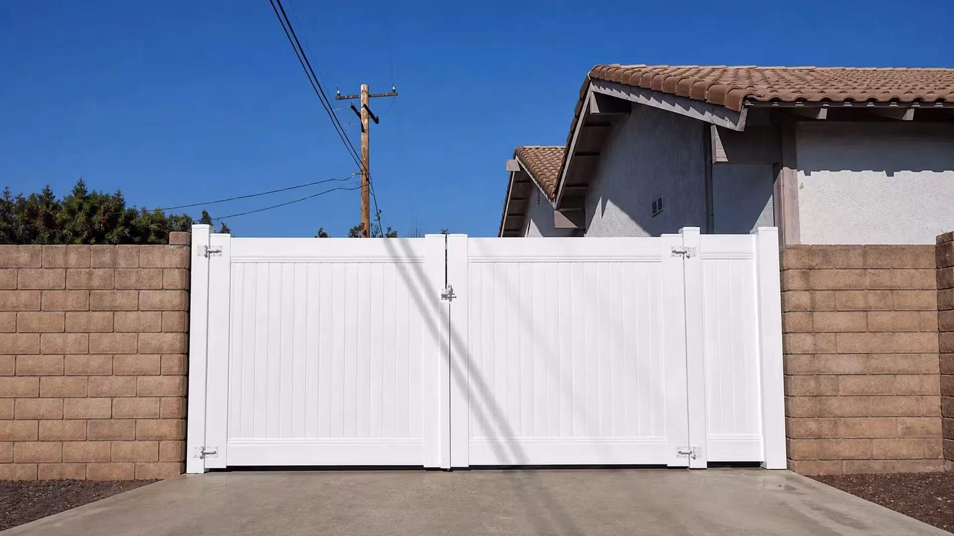 Overhead power lines cross above this vinyl fence gate, finished in White, spanning a masonry driveway opening in Simi Valley