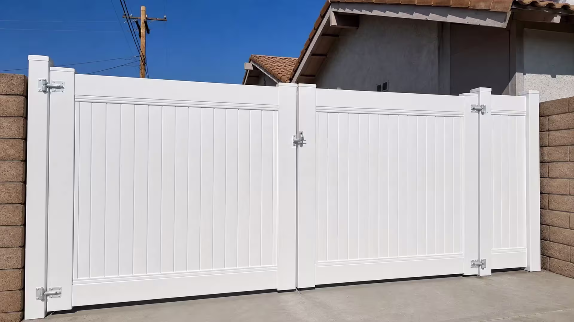 Small wall vents mark the stucco house behind this White vinyl fence gate closing the driveway entrance in Simi Valley
