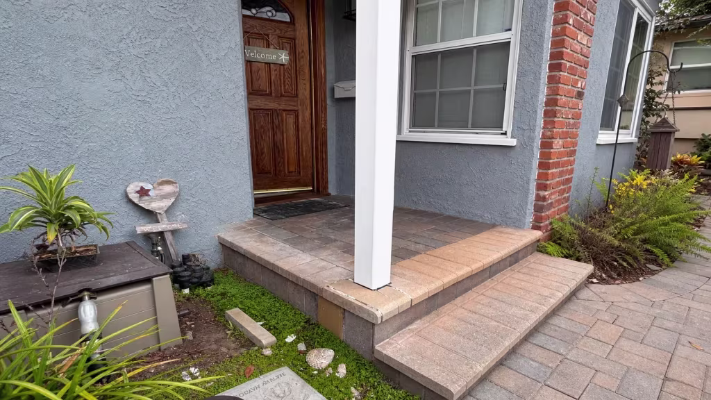 Before installation, the front porch and garden path have brick columns, steps, and planted beds with no fence present.