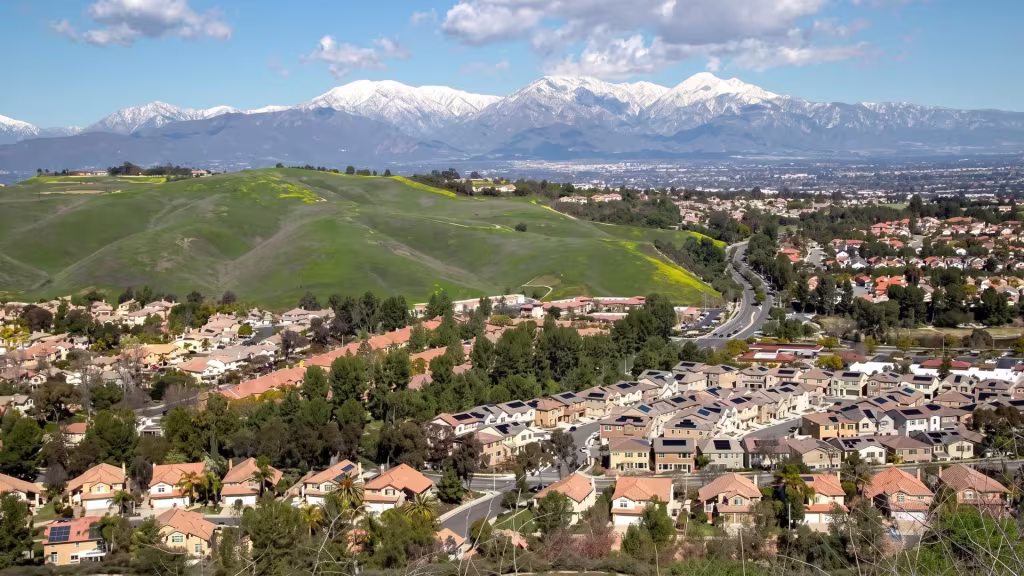 Chino Hills neighborhoods wrap around green hillsides, with snow-capped peaks rising behind them