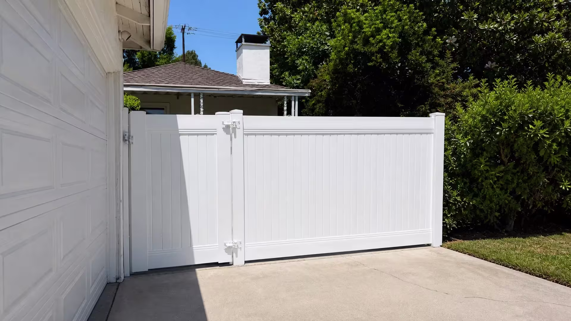 Tall White vinyl privacy fence and gate crossing a concrete driveway beside a shingled roof building in Studio City