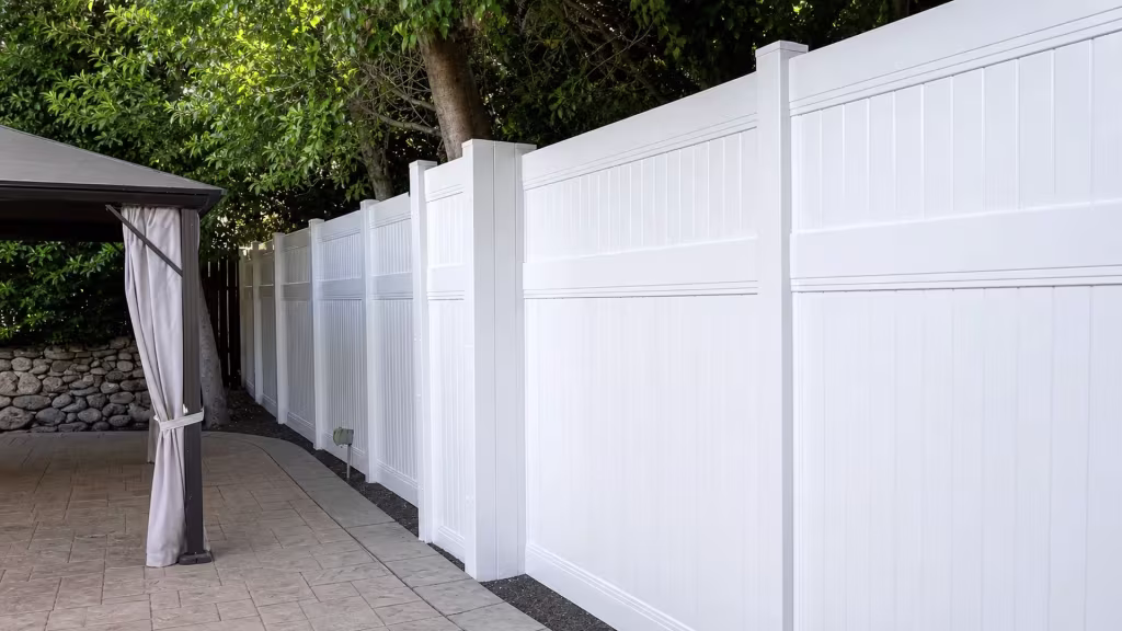 A stamped concrete walkway curves beneath this White vinyl privacy fence under a mature tree canopy in Studio City