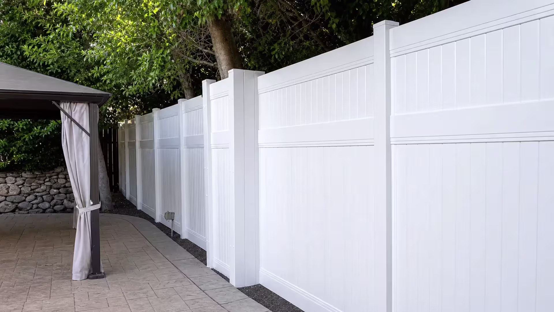 A stamped concrete walkway curves beneath this White vinyl privacy fence under a mature tree canopy in Studio City
