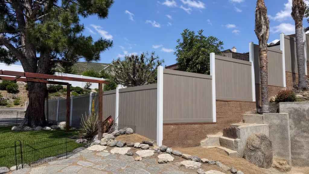 Rounded rocks edge a compacted soil path beside this Weathered Blend vinyl fence climbing a Sylmar hillside yard