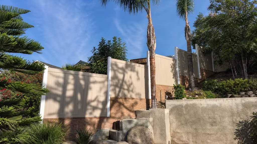 Weathered Blend vinyl privacy fence stepping uphill along a tan retaining wall in Sylmar