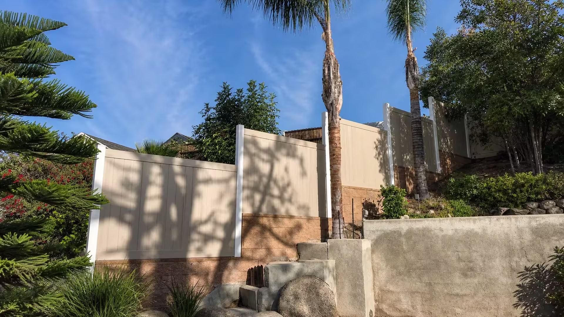 Weathered Blend vinyl privacy fence stepping uphill along a tan retaining wall in Sylmar