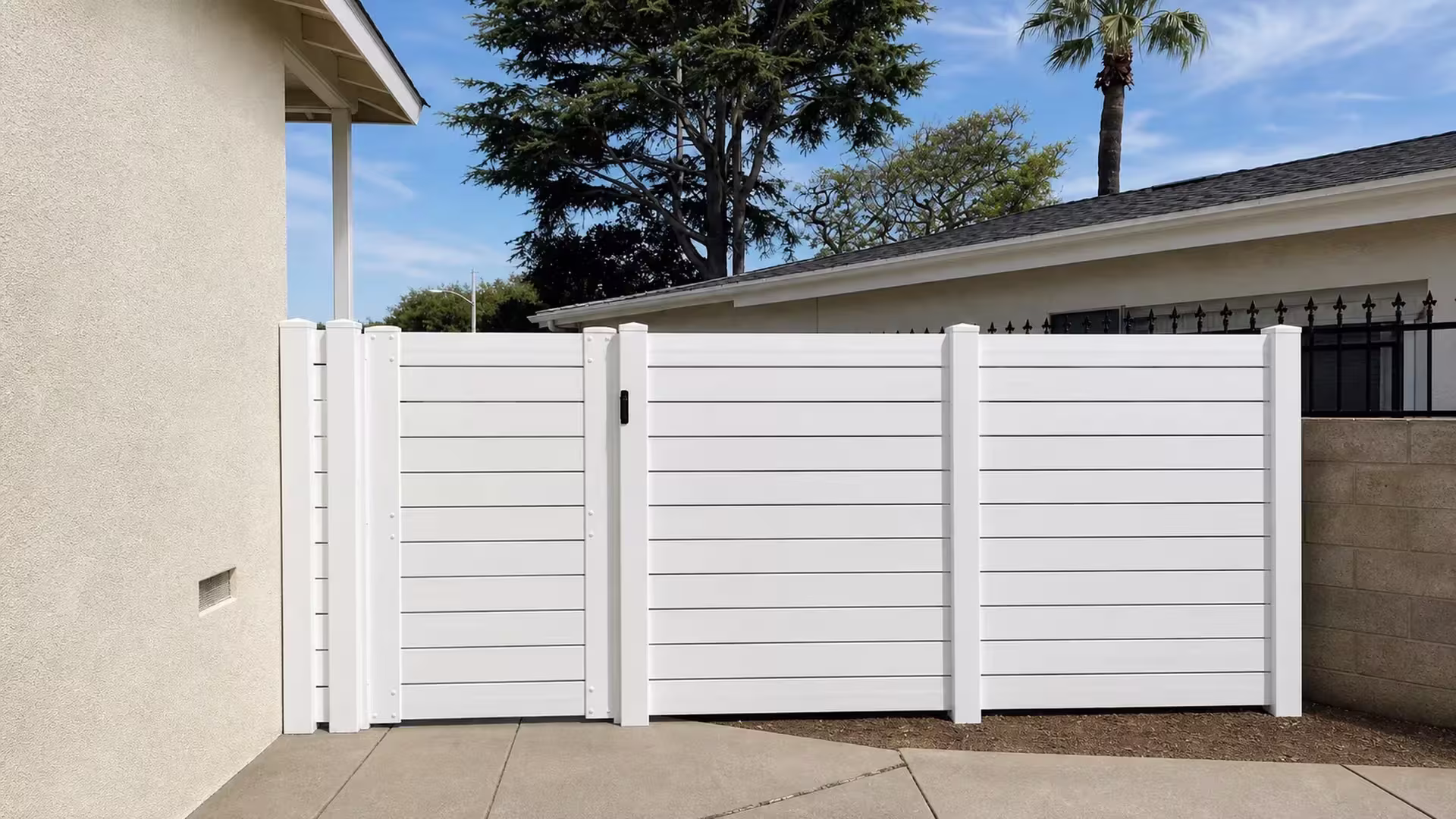 A detached garage anchors one end of this White vinyl horizontal picket fence, which spans a Torrance lawn and patio edge