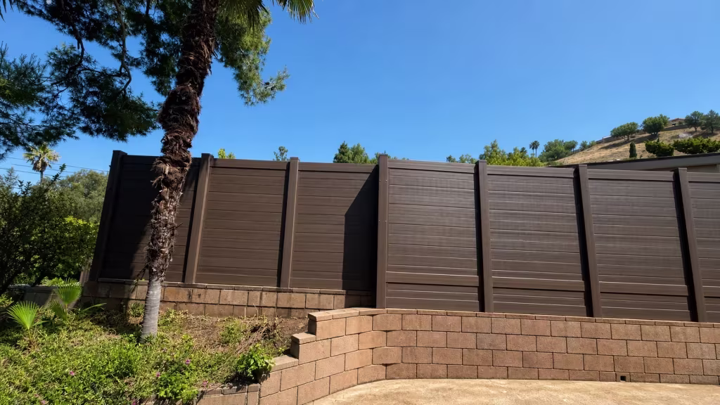 Dark Walnut vinyl privacy fence descends a retaining wall past a crossing palm trunk in Shadow Hills