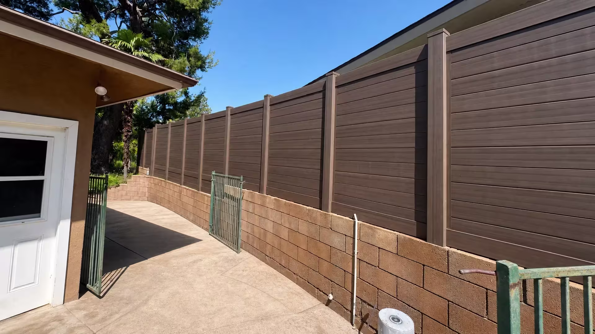 Dark Walnut vinyl privacy fence curving along a retaining wall beside a stucco outbuilding in Shadow Hills