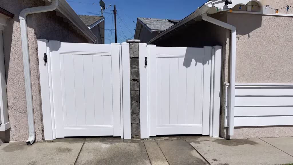 Satellite dishes sit above this Carson side passage, closed by matching White vinyl gates near a block pier